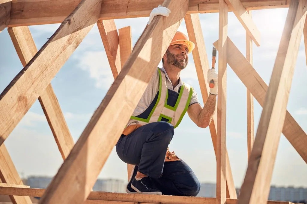 joyous-construction-site-worker-with-hammer-building-a-roof-carcass-1024x682-1.opt.webp
